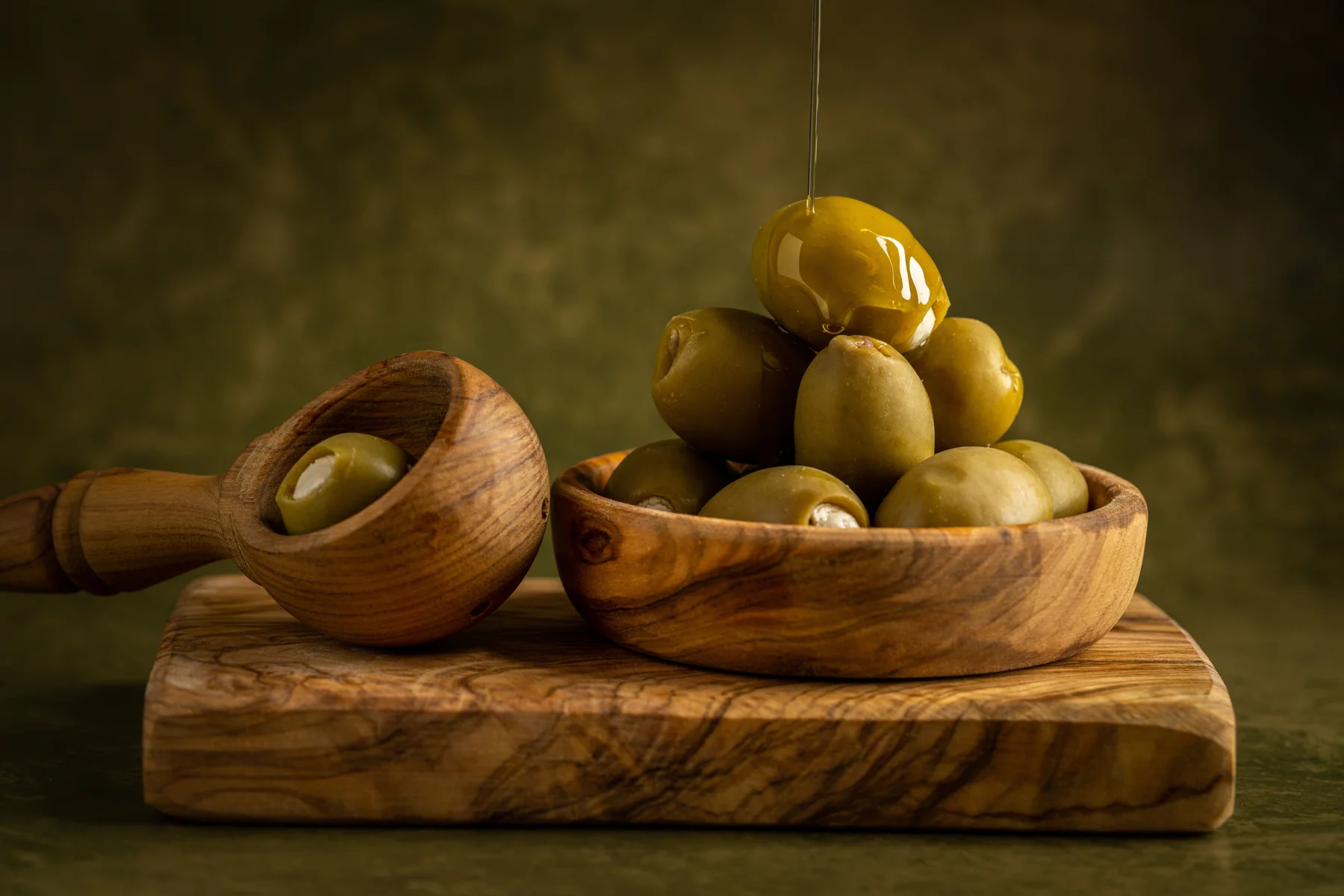 Fresh olive oil poured over green olives in wooden bowls